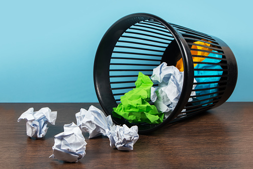 Overturned trash can with crumpled paper balls on a blue background.