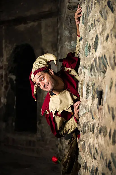 Street performer dressed as joker hide behind a stone wall