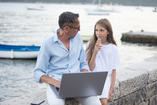 Father and daughter sitting on a beach using laptop