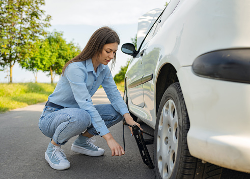 This image portrays proactive roadside maintenance as a young woman uses a car tire jack to ensure tire functionality