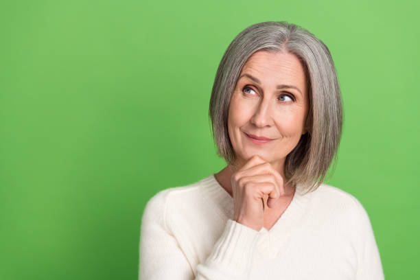 Photo of retired woman grey hair wear trendy white shirt touch chin thoughts look empty space brainstorming isolated on green background Photo of retired woman grey hair wear trendy white shirt touch chin thoughts look empty space brainstorming isolated on green background. deep pick stock pictures, royalty-free photos & images