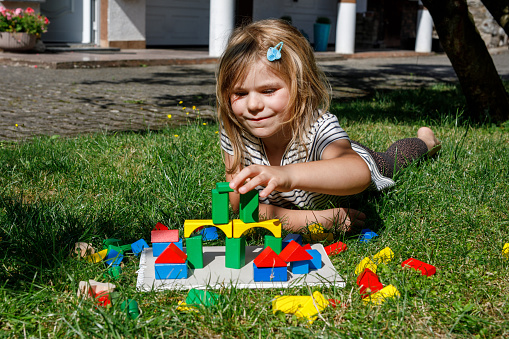 Little preschool girl playing with wooden blocks on the table outdoors. Educational game for small children. Happy child builds a tower from wooden rainbow stacking blocks