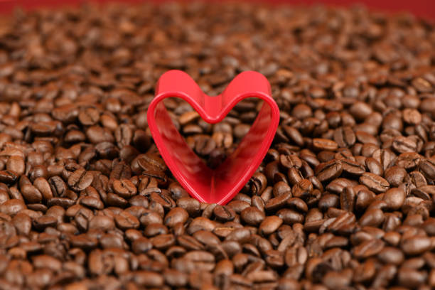 Red heart in roasted coffee beans background. High resolution photo. Soft focus.