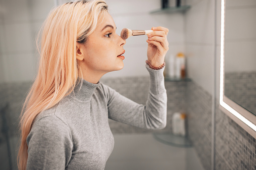 An attractive young Caucasian woman looking herself in the mirror while applying face powder