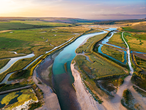 Aerial shot, taken by drone, depicting Cuckmere Haven at sunset in East Sussex, UK. Cuckmere Haven (also known as the Cuckmere estuary) is an area of flood plains in Sussex, England where the river Cuckmere meets the English Channel between Eastbourne and Seaford. The river is an example of a meandering river, and contains several oxbow lakes.