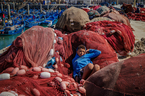 Essaouira, Morocco - August 2, 2023: Picturesque port on the Atlantic coast of Morocco, a child sleeps placidly among the fishing nets laid out on the quay.