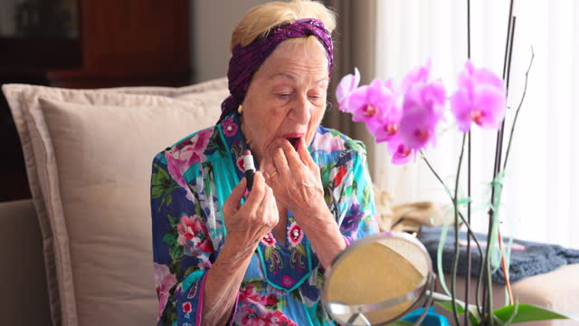 Beautiful senior woman doing makeup in front of mirror at home.