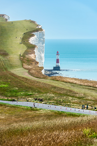Eastbourne, England - July 18, 2020: A tourist walks there on the magnificent white cliffs known as Seven Sisters at low tide, Eastbourne, East Sussex, England.\n\nSquare panoramic.
