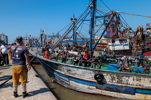 Essaouira, Morocco - August 2, 2023: A fishing vessel returning to port is anchored to the quay with ropes by the fishermen, before unloading its cargo.
