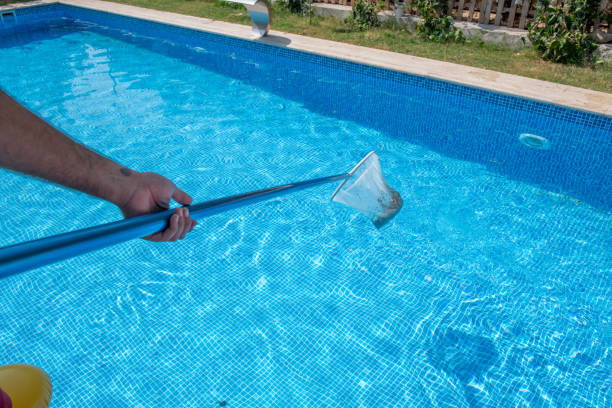 Mature man in flip flops cleaning the swimming pool with a net. Man working as a cleaner of the swimming pool, he standing with special equipment for cleaning at poolside and working