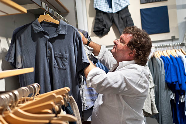 Mature man shopping for a shirt Mature caucasian man shopping for a shirt in a boutique colorful check shirts on sale at a clothing store stock pictures, royalty-free photos & images