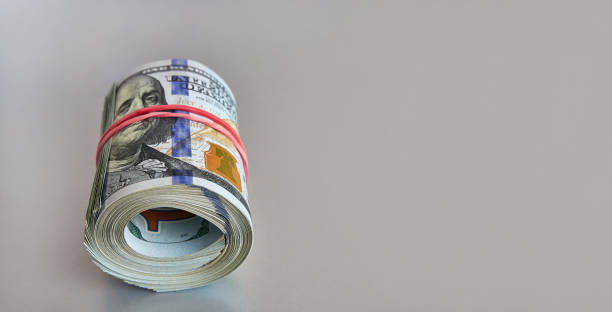 istock Many hundred dollar bills rolled up with a red rubber band on a gray background. 1622911665