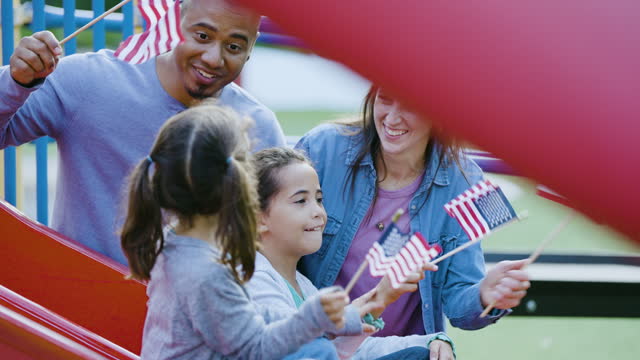 Multiracial family waving American flags on playground