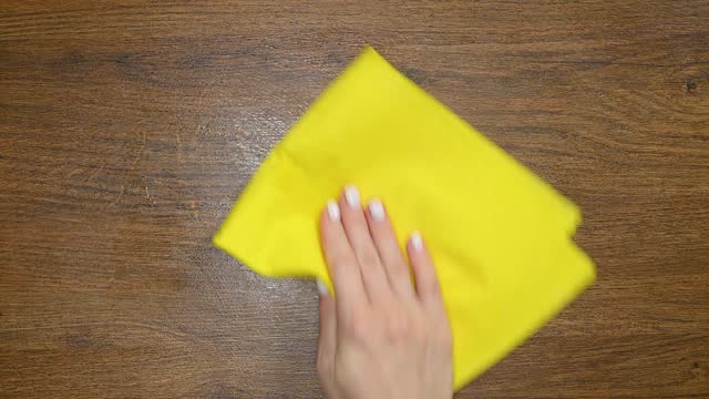 Female hand cleaning table with yellow rag wooden background