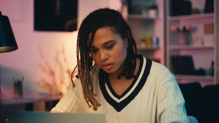 Focused African American writer typing on laptop in the evening, working at home