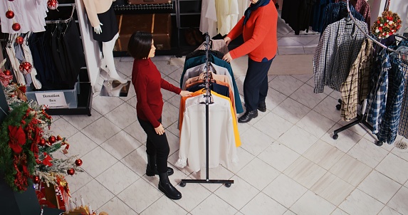 African american man dressed as Santa Claus in Christmas themed shopping mall clothing store. Employee jingling xmas bells and holding red package present in festive decorated shop