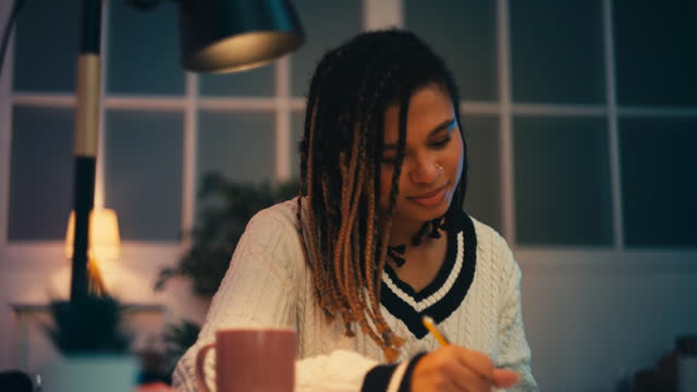 Smiling African American female student doing homework, writing notes at home