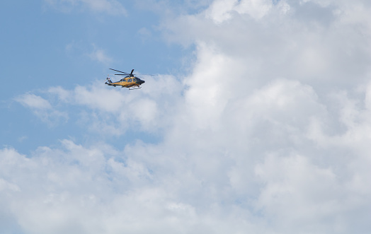 Helicopter flying in the blue sky with white clouds on a sunny day.