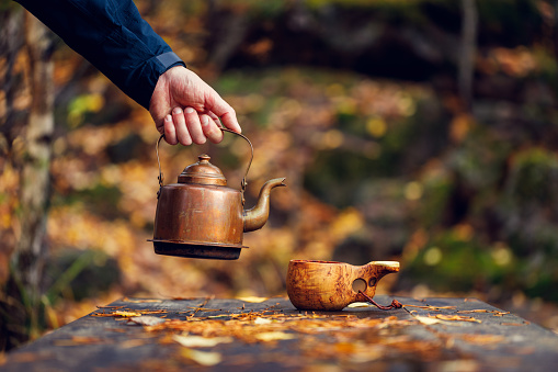 A man brews delicious coffee in the autumn forest. Background is blurred.