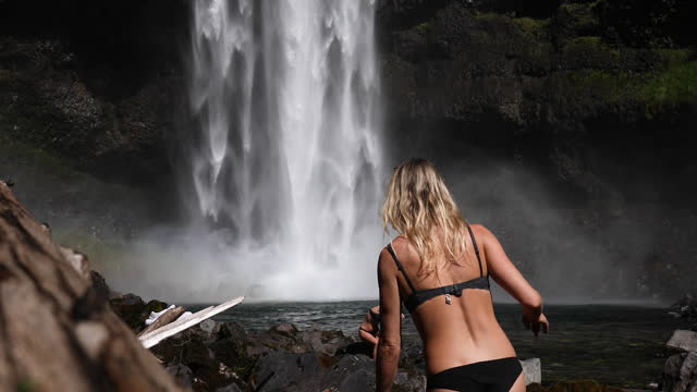 Two young women look up to towering waterfall