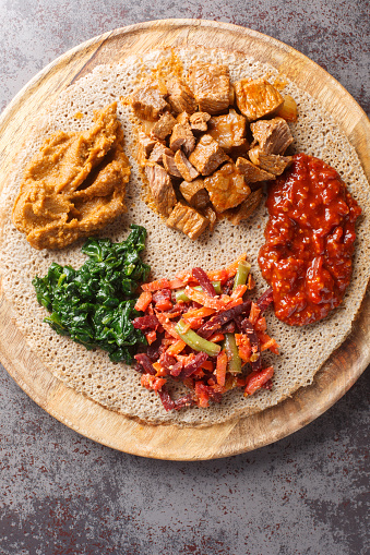 Mix of vegetables and stews on injera flatbread close up on the wooden board on the table. Vertical top view from above