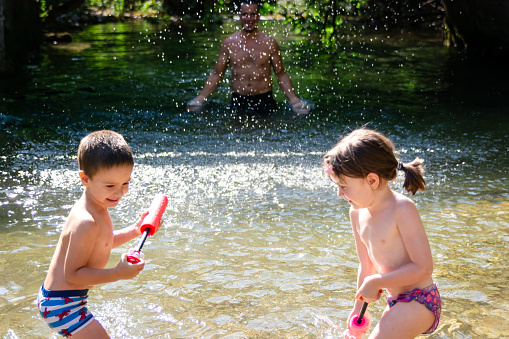 Father playing whit his children on the river during summer day