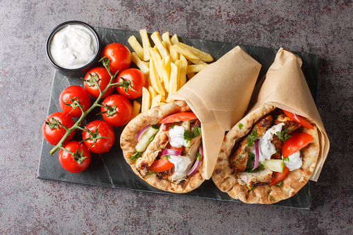 Chicken gyros with vegetables, french fries and tzatziki sauce closeup on the board on the table. Horizontal top view from above