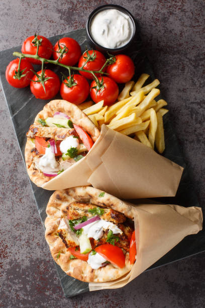 Tasty wrapped greek chicken gyros with vegetables, french fries and tzatziki sauce closeup on the board. Vertical top view stock photo