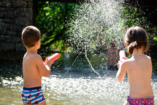 Rear view of two happy kids playing whit water on the river during summer day