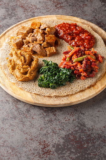 Meal consisting of injera and several kinds of wat or tsebhi stew is typical of Ethiopian cuisine closeup on the wooden board. Vertical