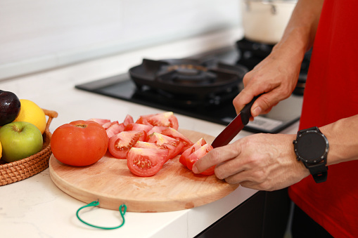 Cropped image of an Asian mid-aged man slicing tomatoes for juice, as he prepares healthy food in the kitchen after his workout.