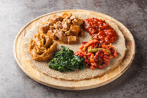 Injera is a sourdough flatbread made from teff flour served with filling close up on the wooden board on the table. Horizontal