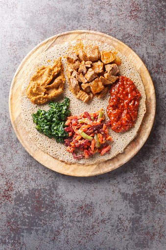 Meal consisting of injera and several kinds of wat or tsebhi stew is typical of Ethiopian cuisine closeup on the wooden board. Vertical top view from above