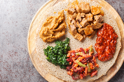 Ethiopian Injera flat bread with various vegetable and meat fillings close up on the wooden board on the table. Horizontal top view from above