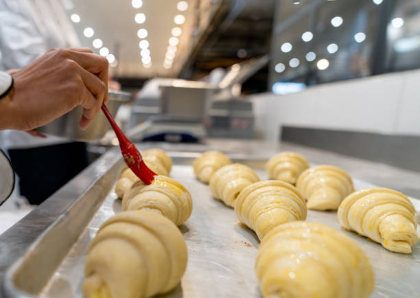 Close-up on a baker spreading egg yolks on some croissants while working at the bakery