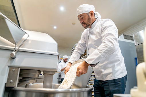 Latin American baker mixing flour while making bread at the bakery - small business concepts