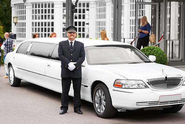 Commuting in luxury A proud chauffeur standing beside a white stretch limousine luxury hotel stock pictures, royalty-free photos & images