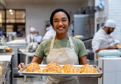 istock Happy woman working at a bakery holding a tray of fresh bread 1623084547