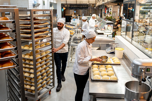 Group of Latin American employees working at a bakery baking fresh bread - small business concepts