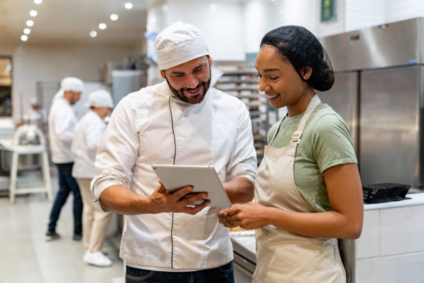 Baker training a new employee at the bakery Baker training a new employee at the bakery and using a digital tablet - small business concepts restaurant kitchen workers stock pictures, royalty-free photos & images