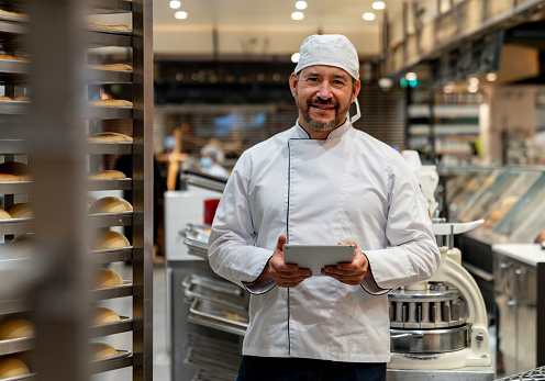 Happy Latin American business owner managing a bakery and using a digital tablet