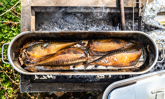 top view of freshly smoked fish in open steel smoking pot on outdoor charcoal grill on sunny summer day