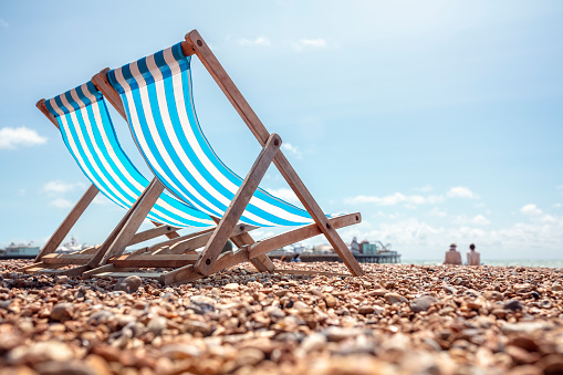 Blue Deckchair on a pebble beach at the seaside near a pier on summer vacation