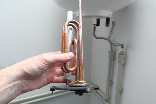 master installs a new electric heating ten in a water tank