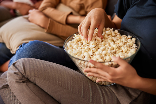 Close-up of female person sitting on a couch eating popcorn.