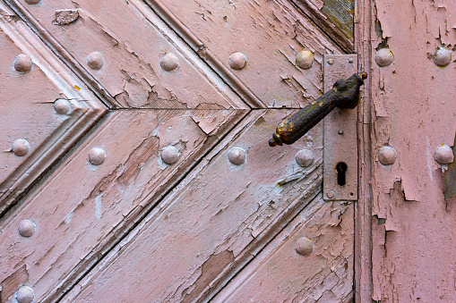 close-up of an old, wooden door with a handle and keyhole. The door is made from planks of wood that have been weathered by the elements over time, giving it a rustic look.