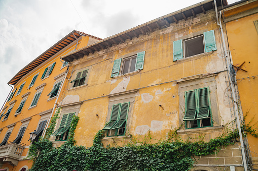 Low angle view of exterior of rustic yellow traditional residential building with ivy growing on wall in old town at Pisa, Italy