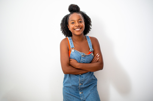 Portrait of cute smiling teenage african girl with arms crossed leaning to white background
