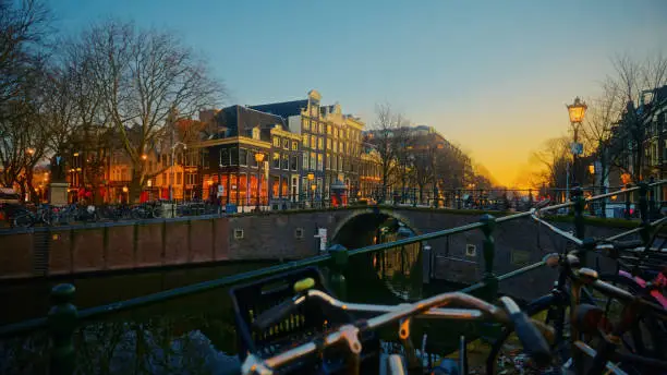 Bicycles parked on railing of stunning arch bridge and beautiful architecture of Amsterdam city at night