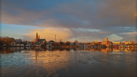 Experience the stunning beauty of Zaanse Schans during sunrise with this image of a riverside town surrounded by charming residential buildings. The perfect blend of old-world charm and natural beauty,capturing the essence of traditional Dutch architecture.